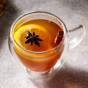 Overhead view of a Rum Hot Toddy cocktail in a glass mug on a gray countertop with a cinnamon stick, star anise and lemon slice in the glass as a garnish.