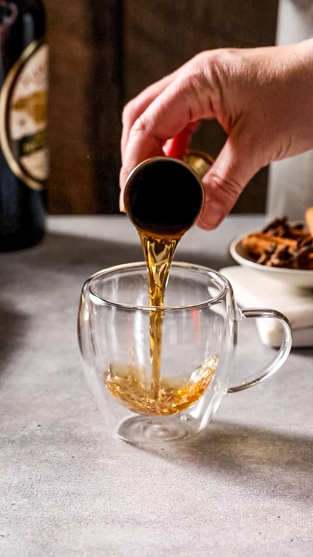 Hand pouring dark rum from a jigger into a glass mug.