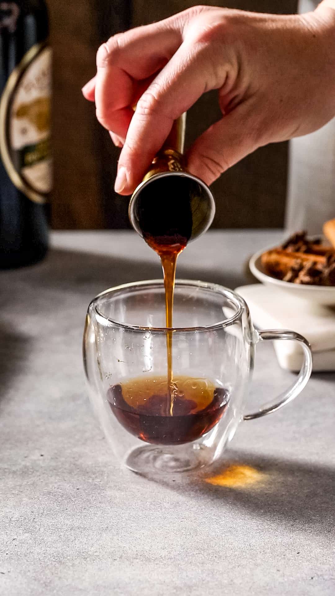 Hand pouring honey from a jigger into a glass mug.