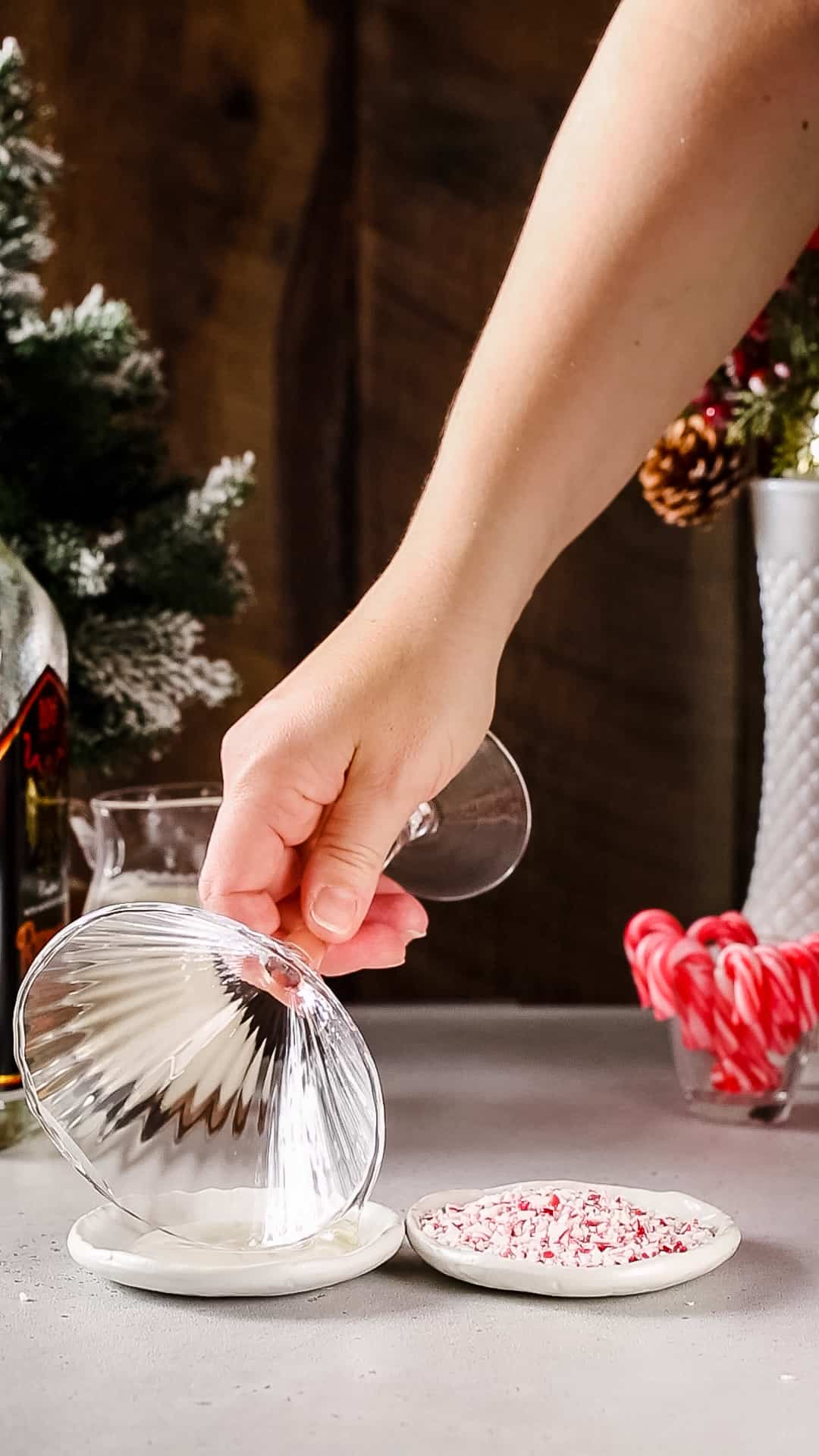 Hand dipping the rim of a tall ridged martini glass into a dish of corn syrup.
