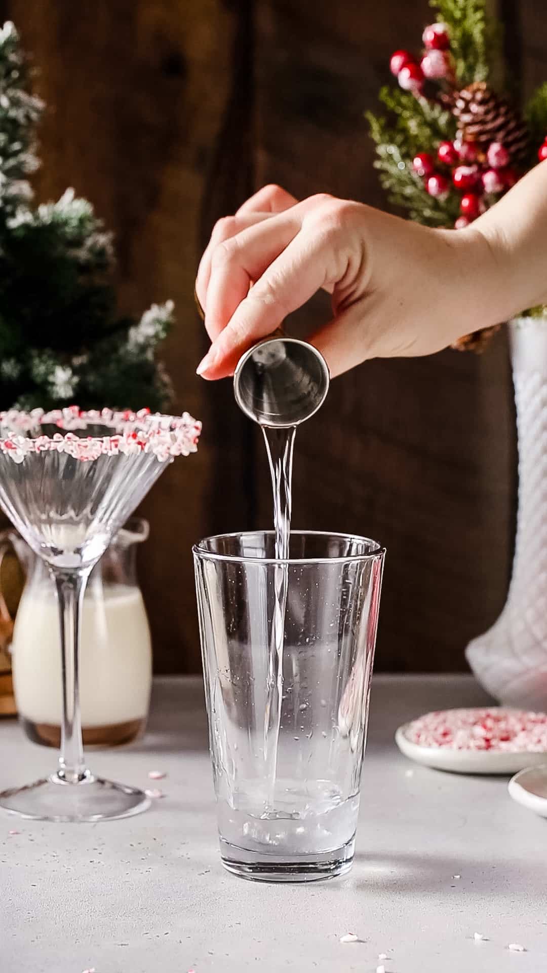 Hand pouring peppermint schnapps liqueur from a jigger into a cocktail shaker.