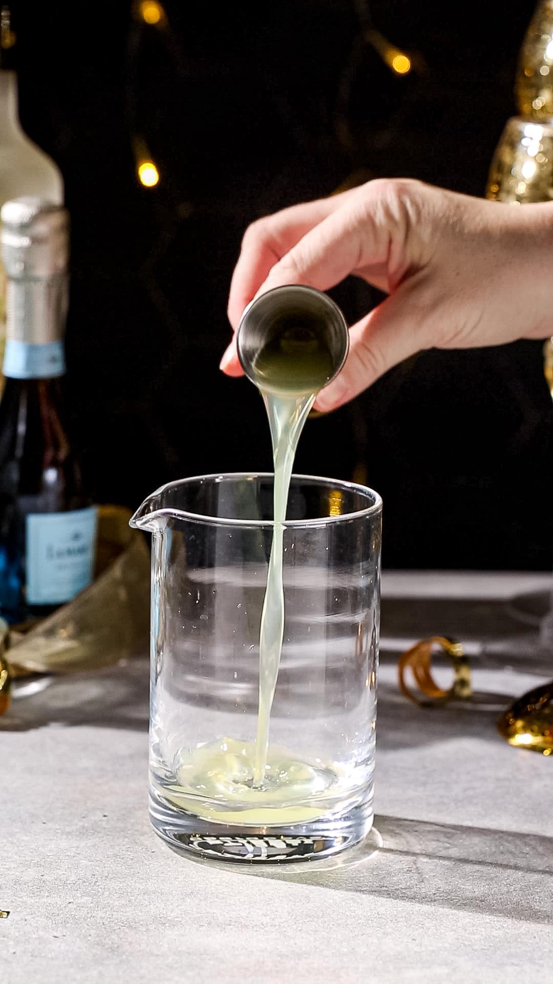 Hand pouring limoncello liqueur from a cocktail jigger into a mixing glass.