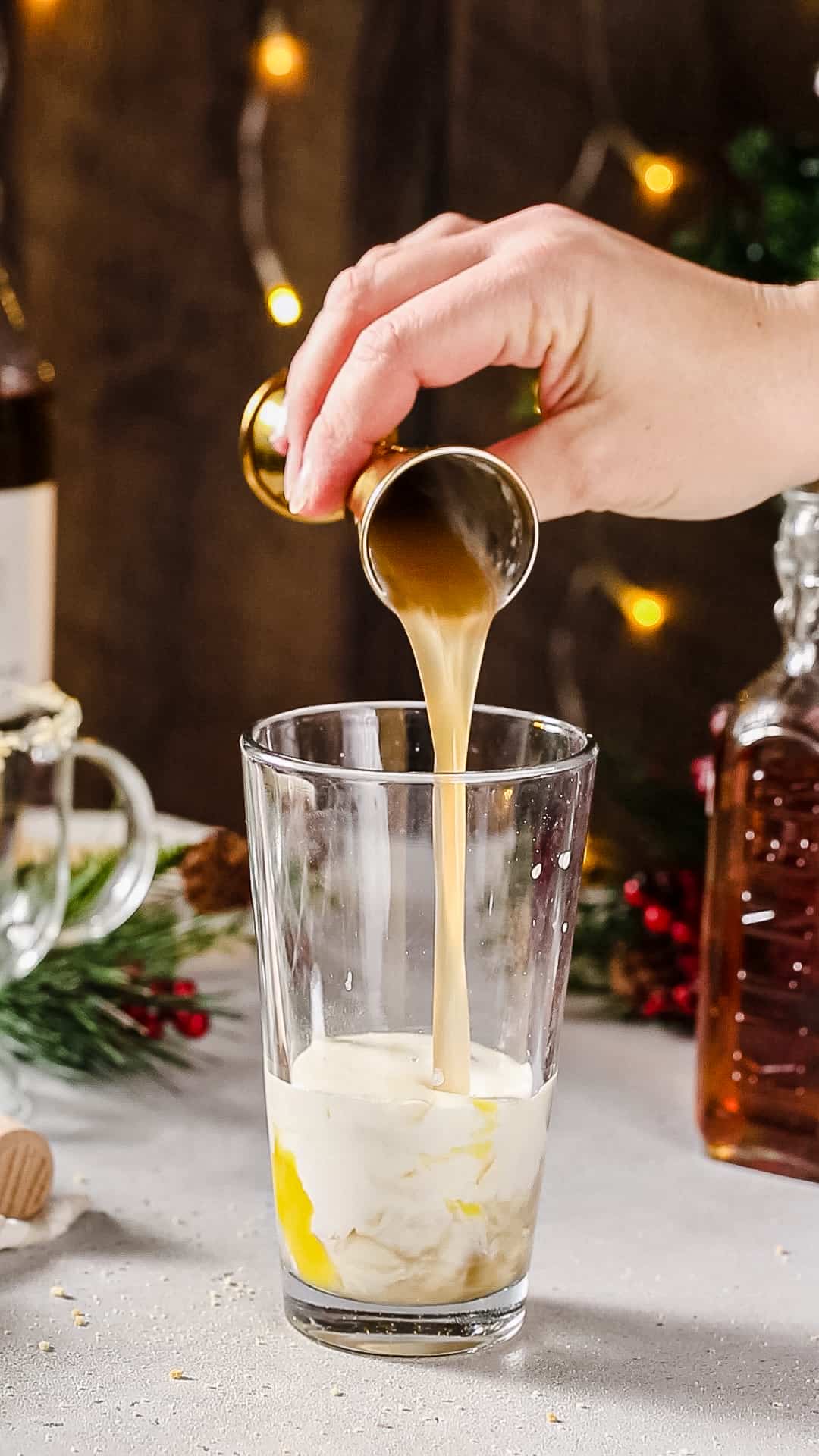 Hand pouring sugar cookie syrup from a jigger into a cocktail shaker.