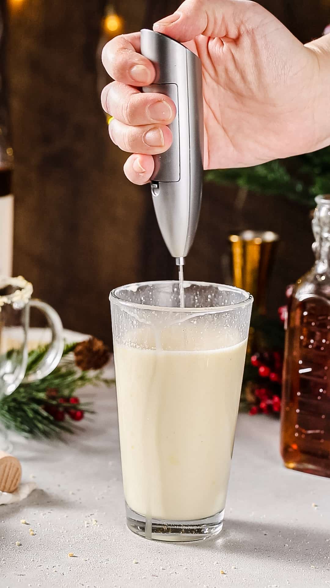 Hand using a milk frother to whip up the creamy cocktail in a cocktail shaker.