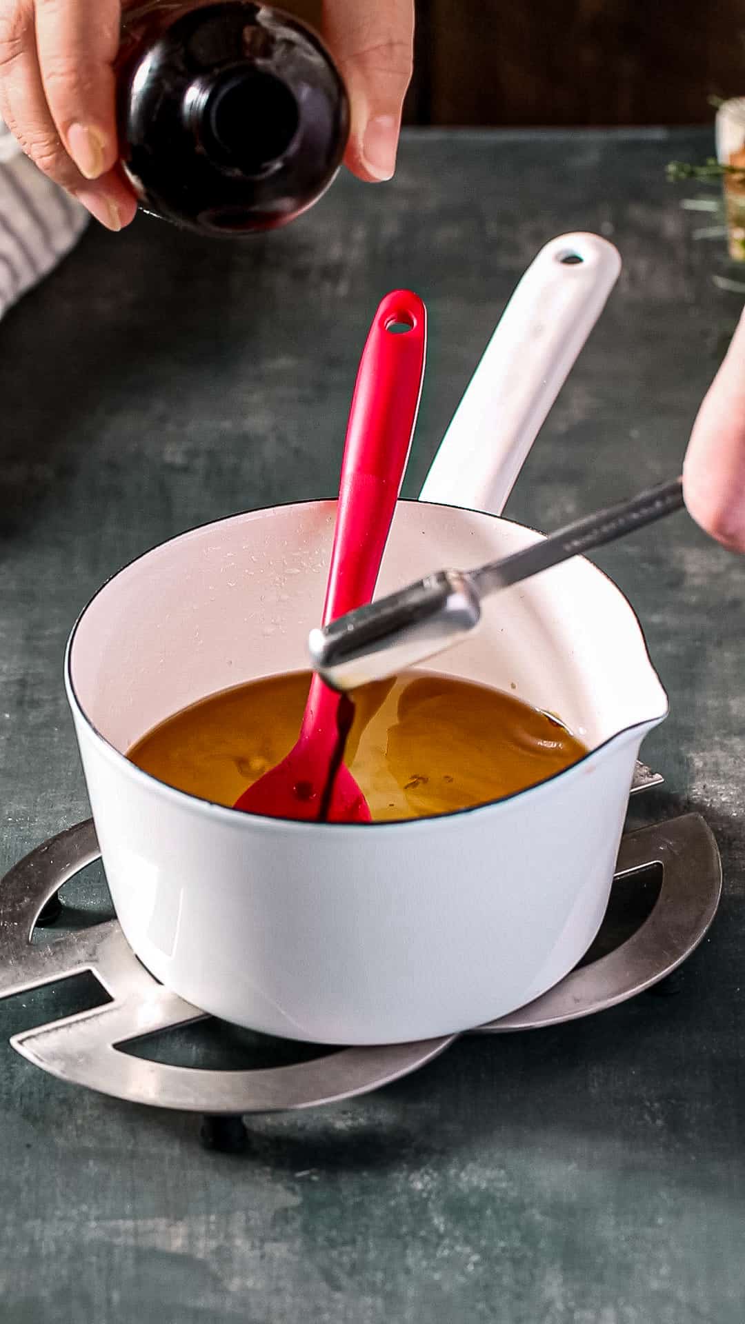 Hand adding vanilla extract to a white pot.