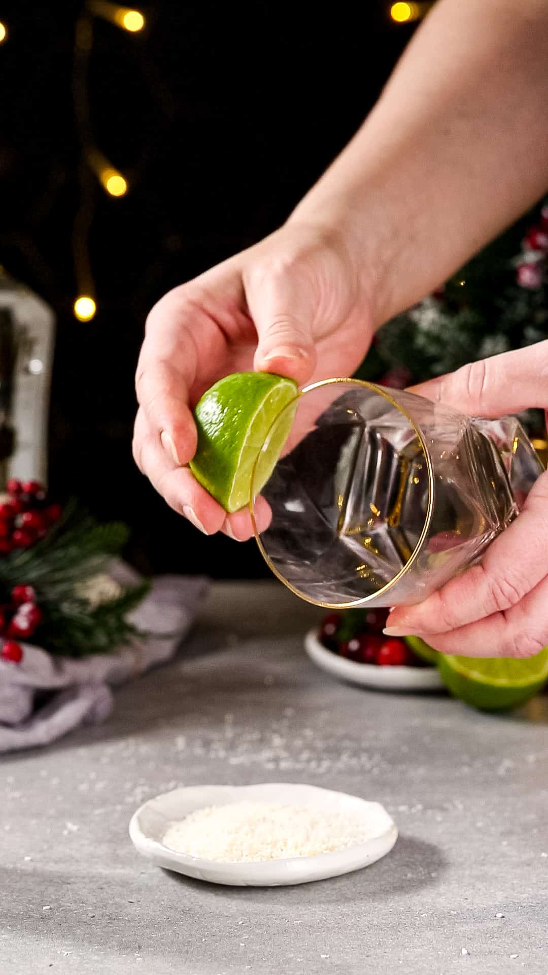 Hand using a cut lime to wet the rim of a cocktail serving glass.
