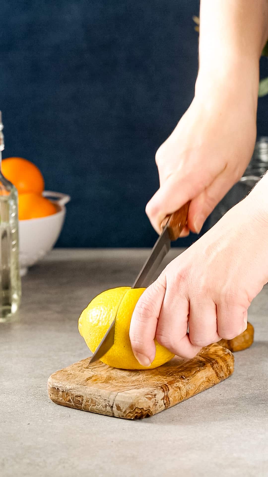 Hands cutting a lemon on a small wooden cutting board.