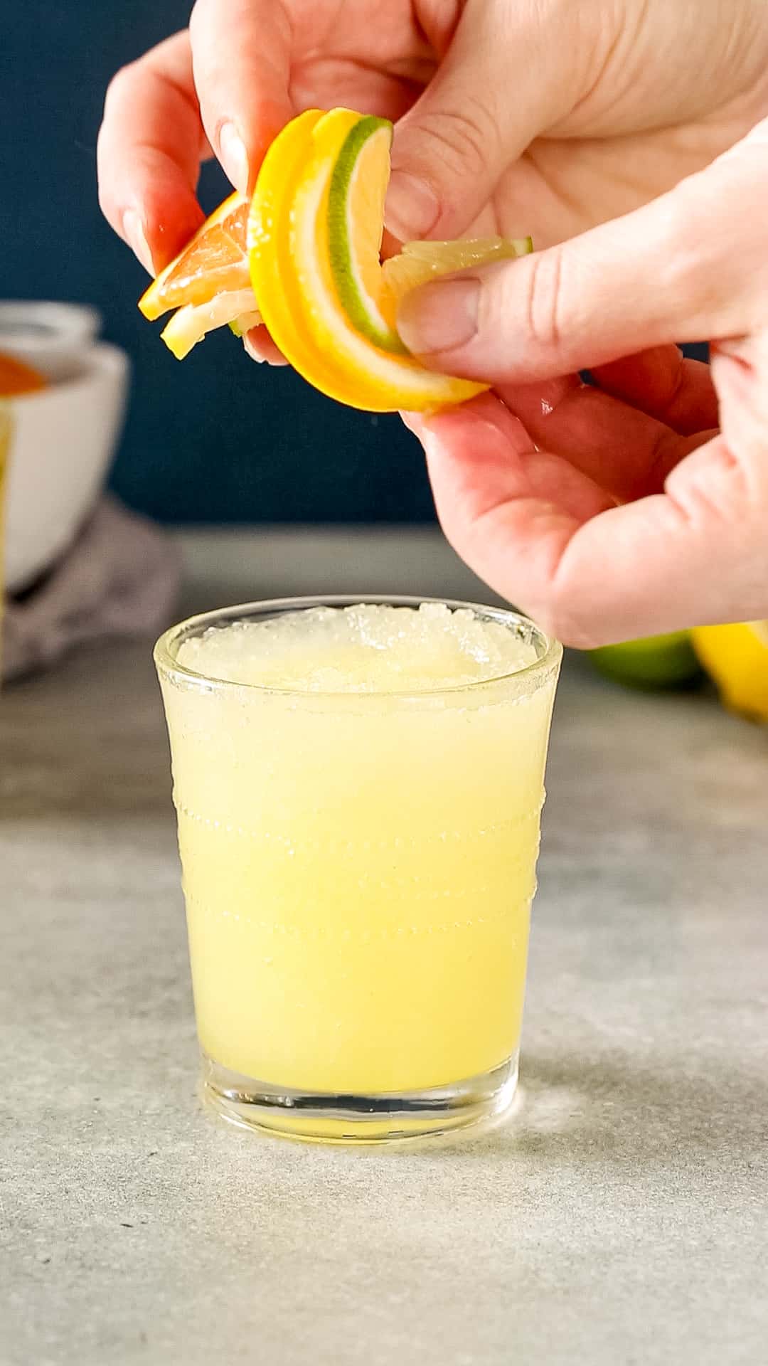 Hands twisting together citrus slices to add to the top of a yellow slush drink.