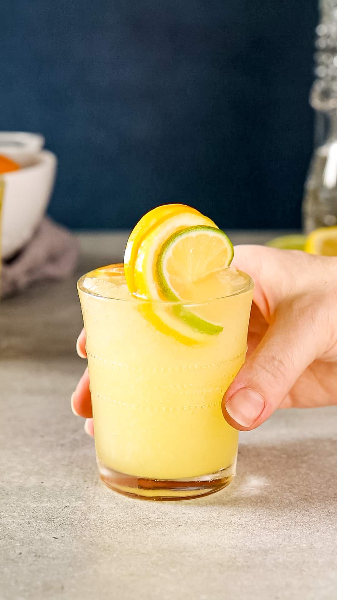 Hand about to pick up a Citrus Slush mocktail from a gray countertop.