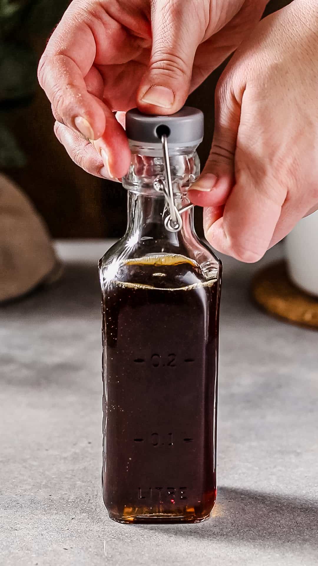 Hands closing up a glass swing-top bottle filled with brown liquid.