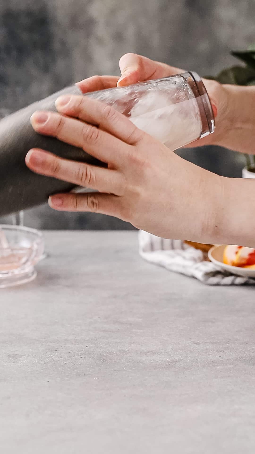 Hands shaking a gray metal and glass cocktail shaker filled with liquid and ice.