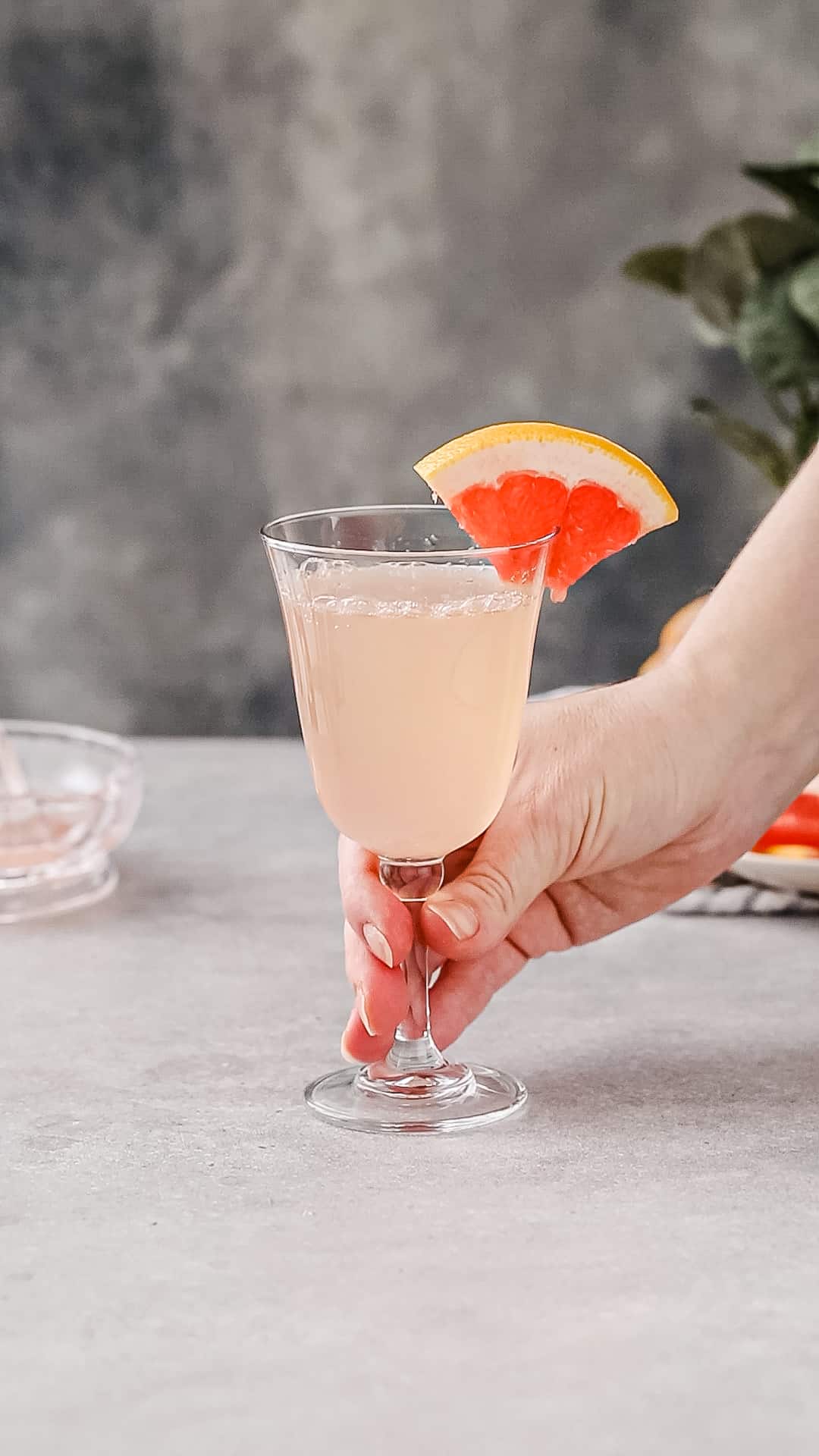 Hand about to pick up a grapefruit mocktail that is sitting on a gray countertop.