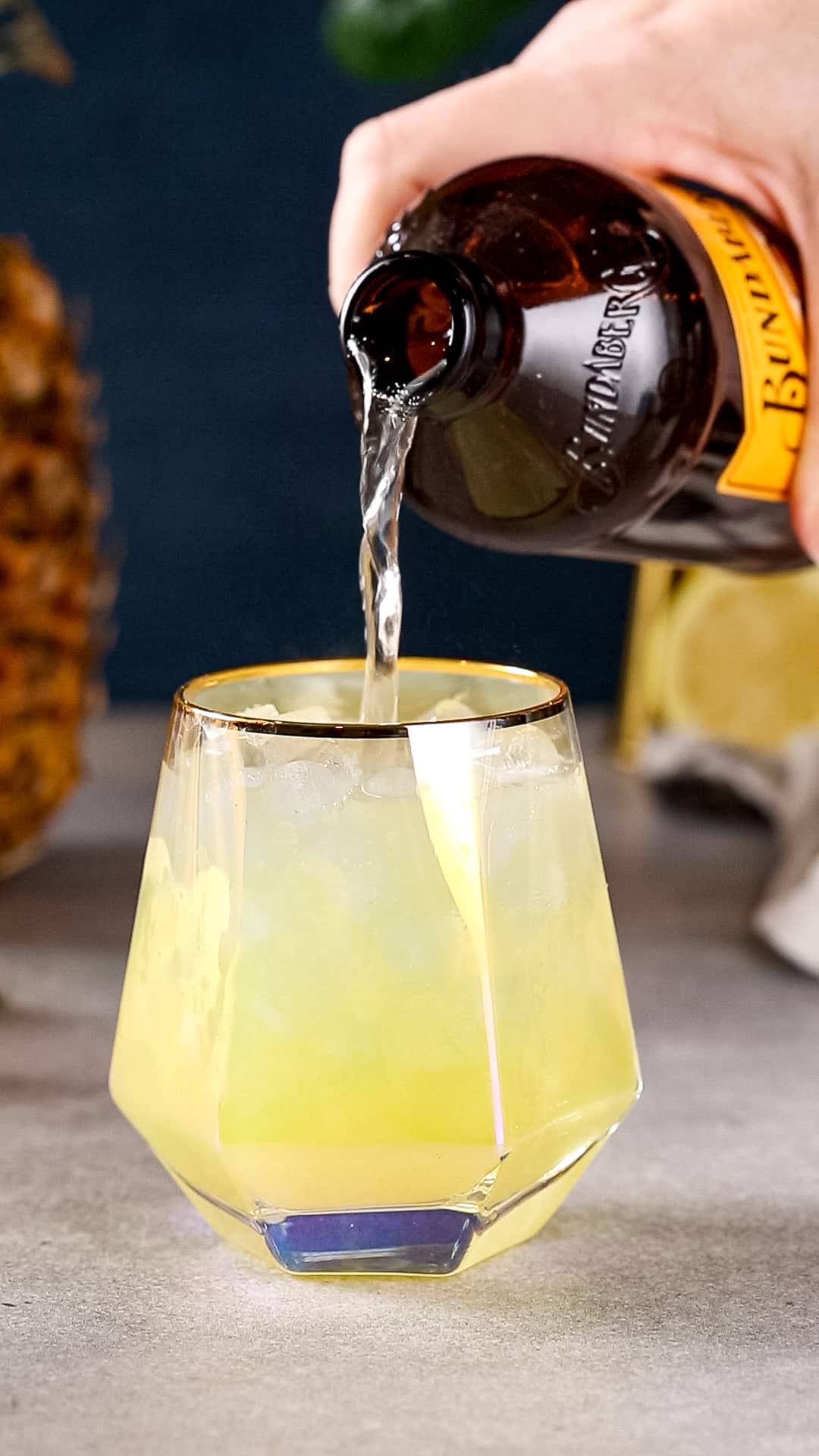 Hand pouring ginger beer into a cocktail serving glass.