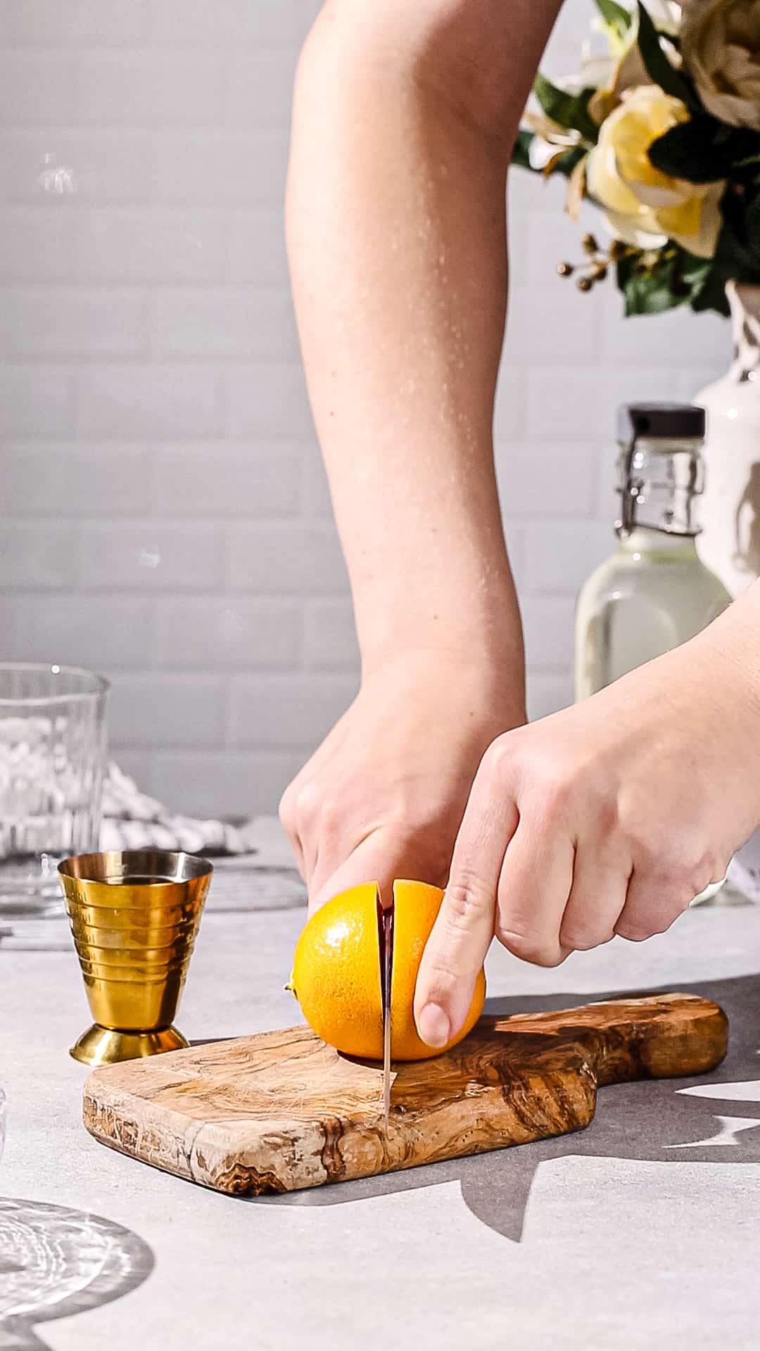 Hands using a knife and cutting board cutting a lemon in half.