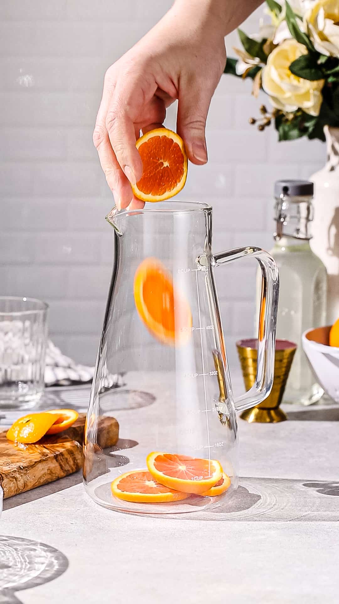 Hand adding orange slices to a glass pitcher.