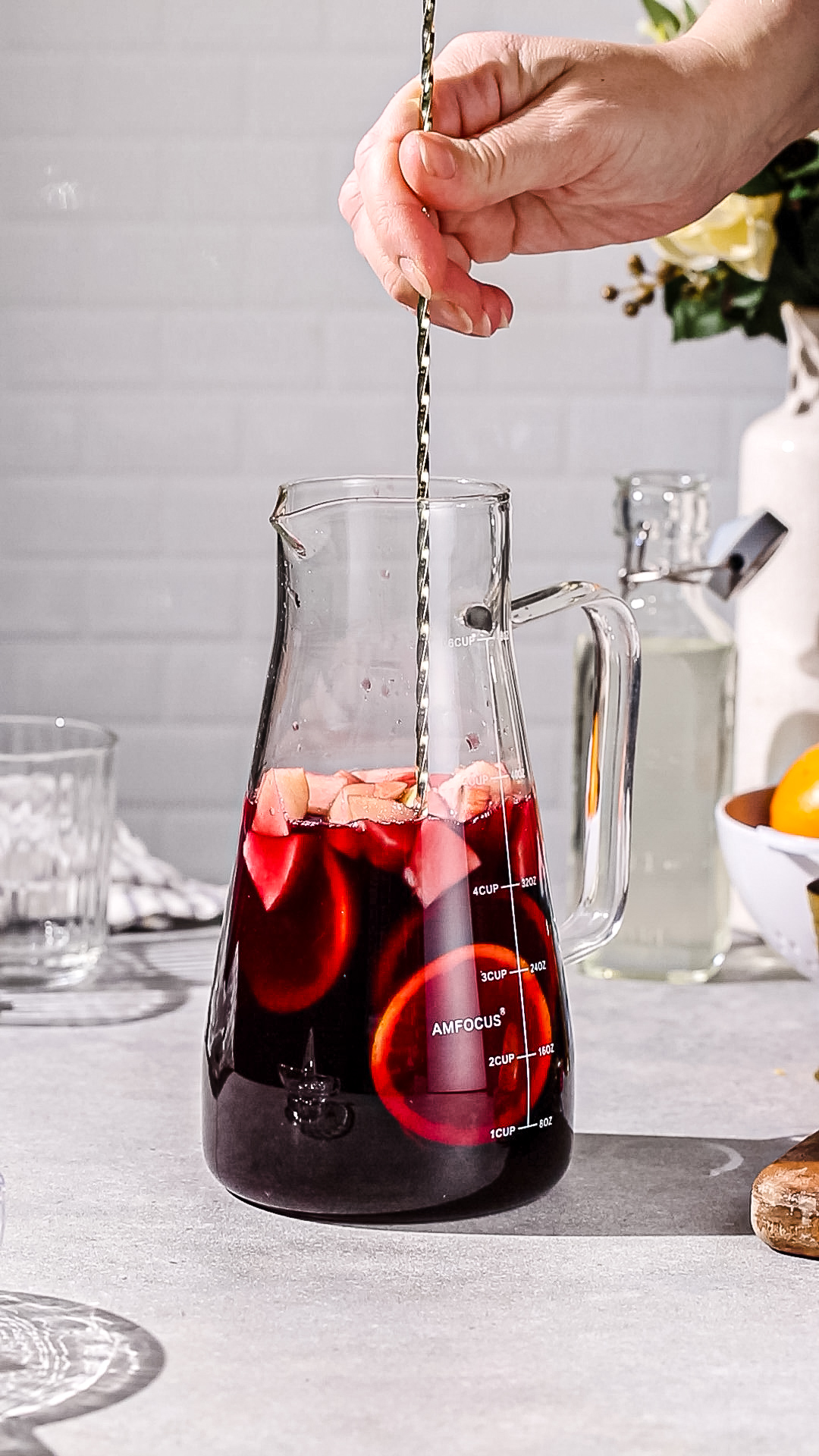 Hand using a long bar spoon to stir a pitcher of non-alcoholic sangria.