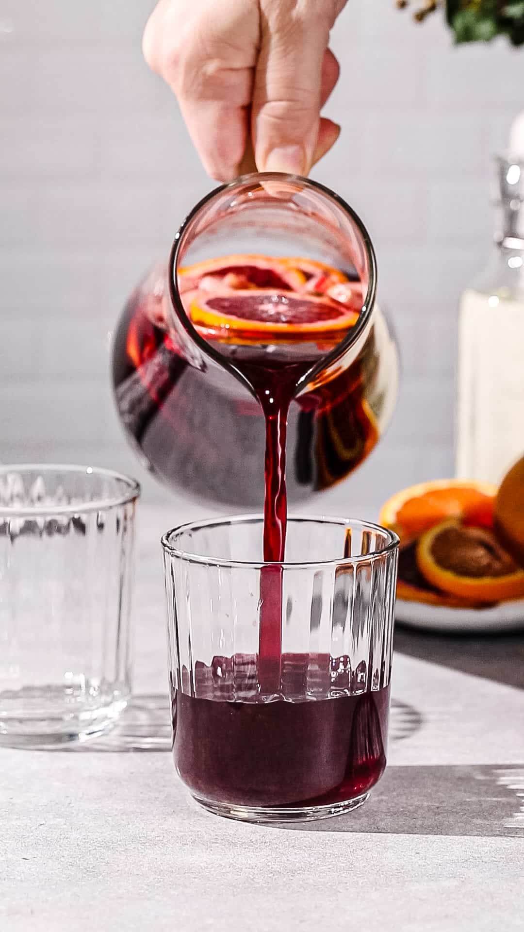 Hand using a glass pitcher to pour non-alcoholic sangria into a lowball glass.