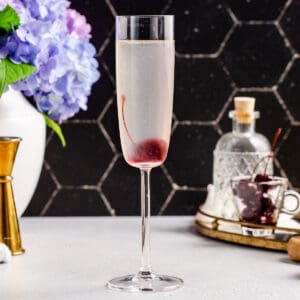 Side view of French 76 cocktail in a champagne flute with a cherry garnish in the bottom of the glass.