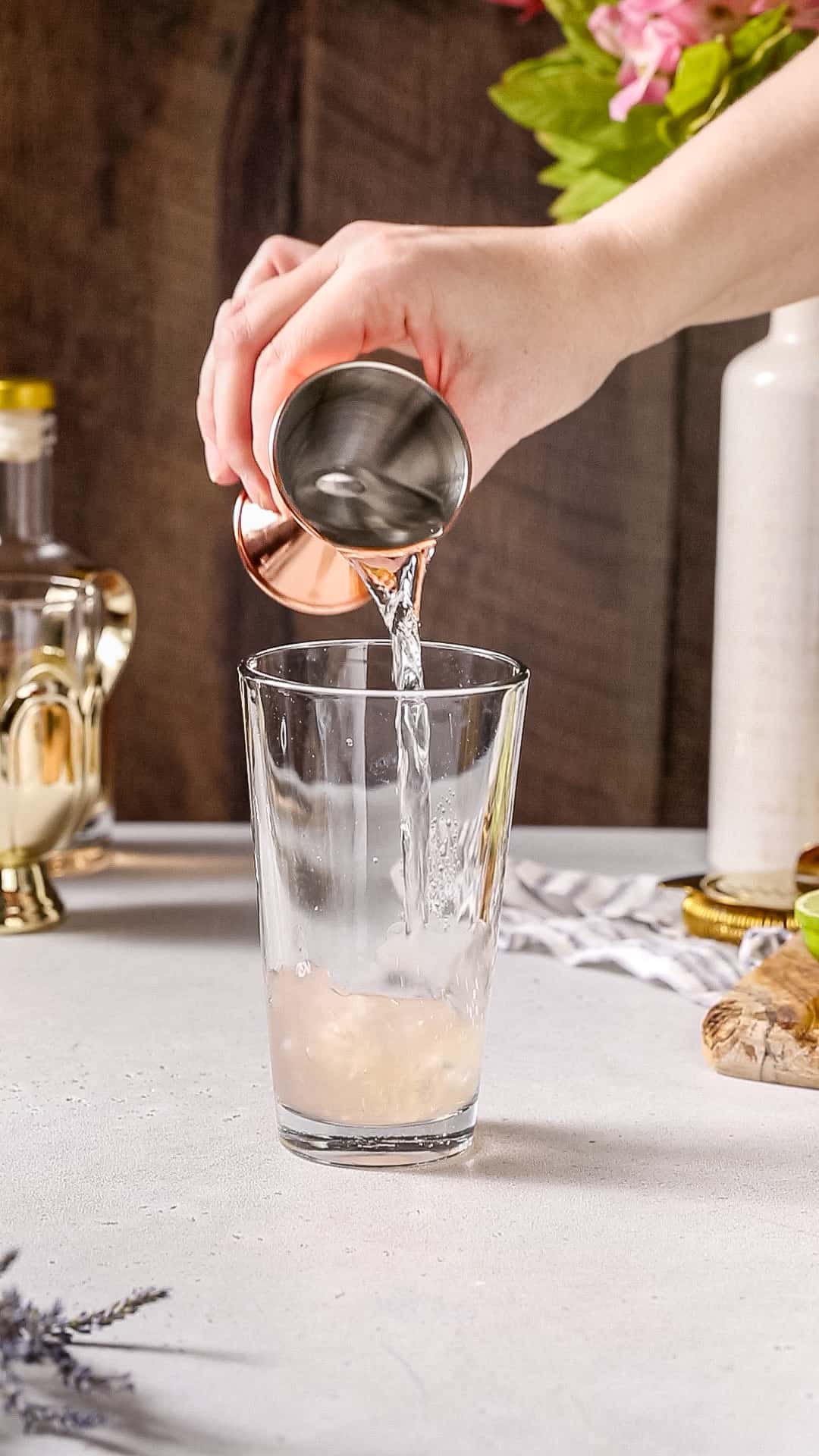 Hand pouring vodka from a jigger into a cocktail shaker.