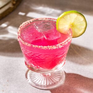 Pink colored prickly pear margarita in a salt rimmed glass garnished with a lime wheel.
