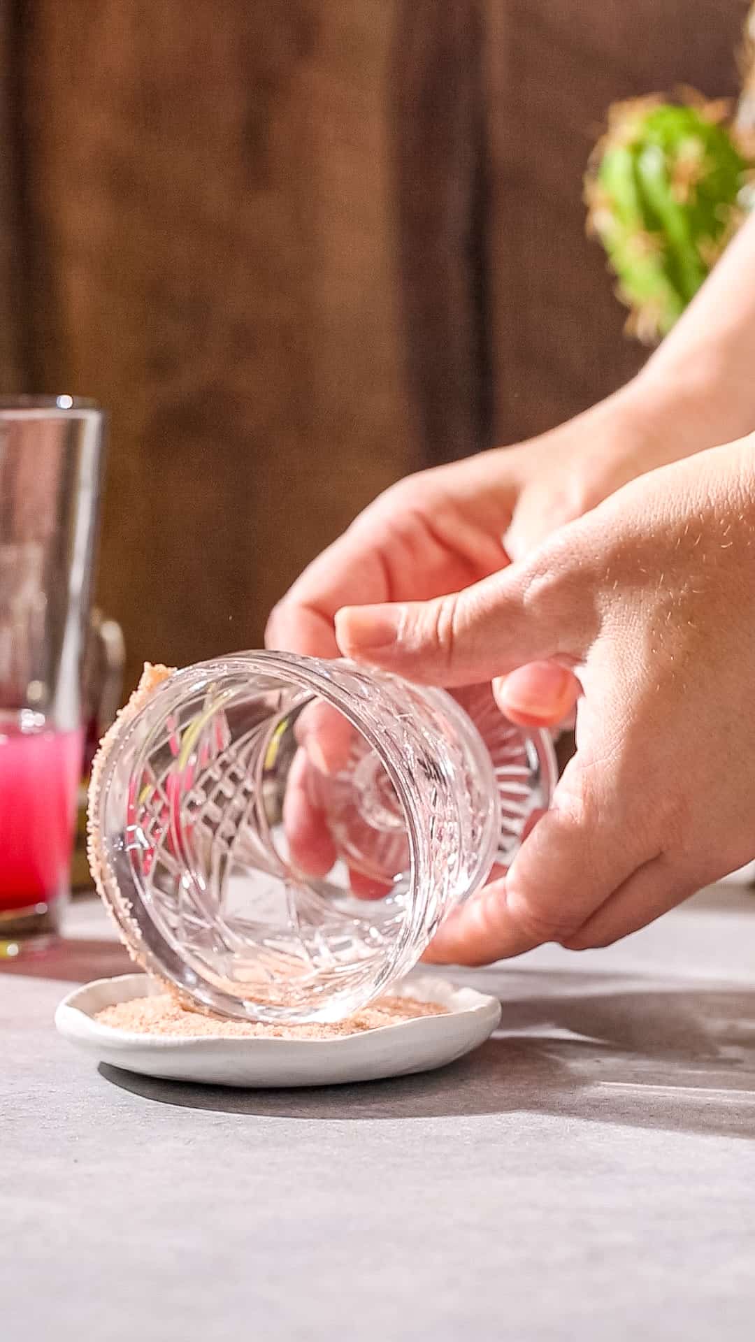 Hands dipping the rim of a cocktail glass into a dish of Himalayan pink salt.