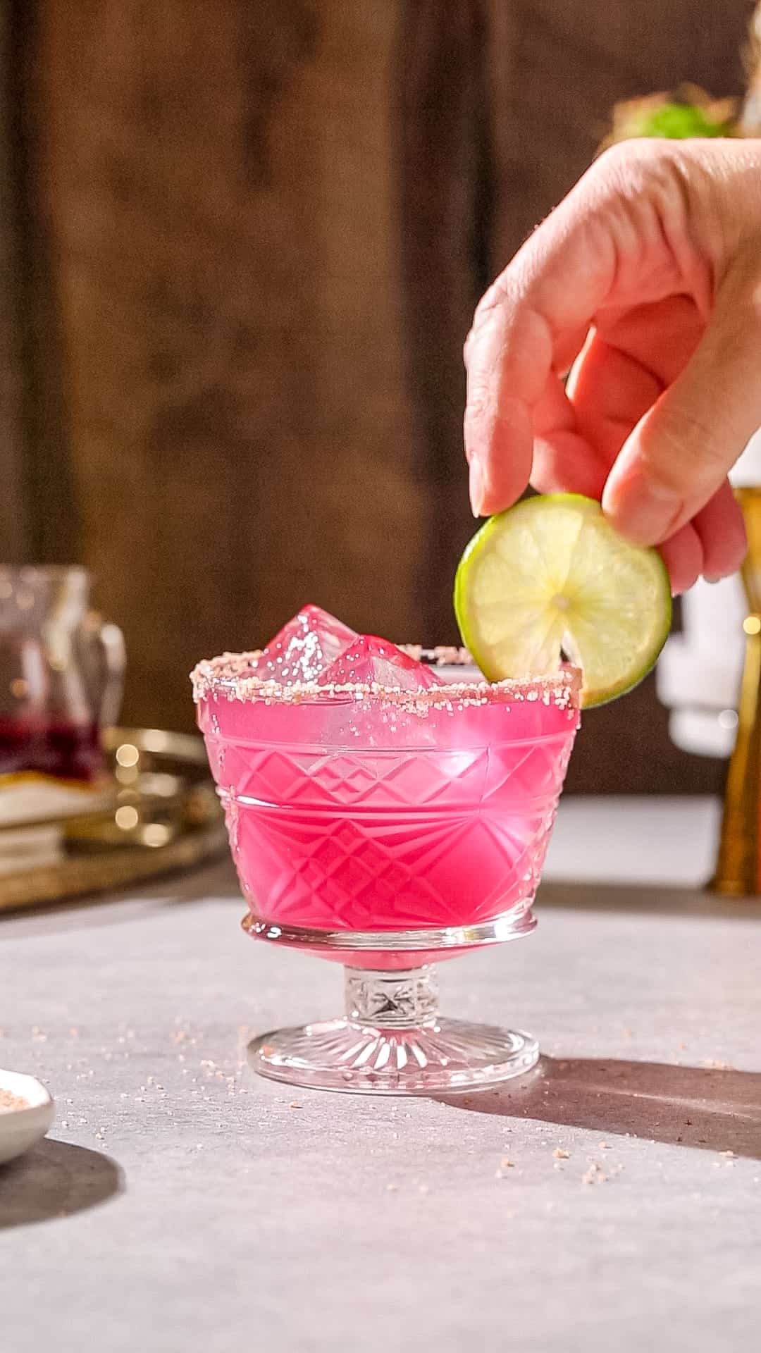 Hand adding a lime wheel garnish to a prickly pear Margarita cocktail.