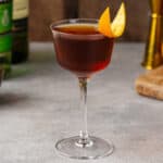Tipperary cocktail on a gray countertop garnished with an orange peel.