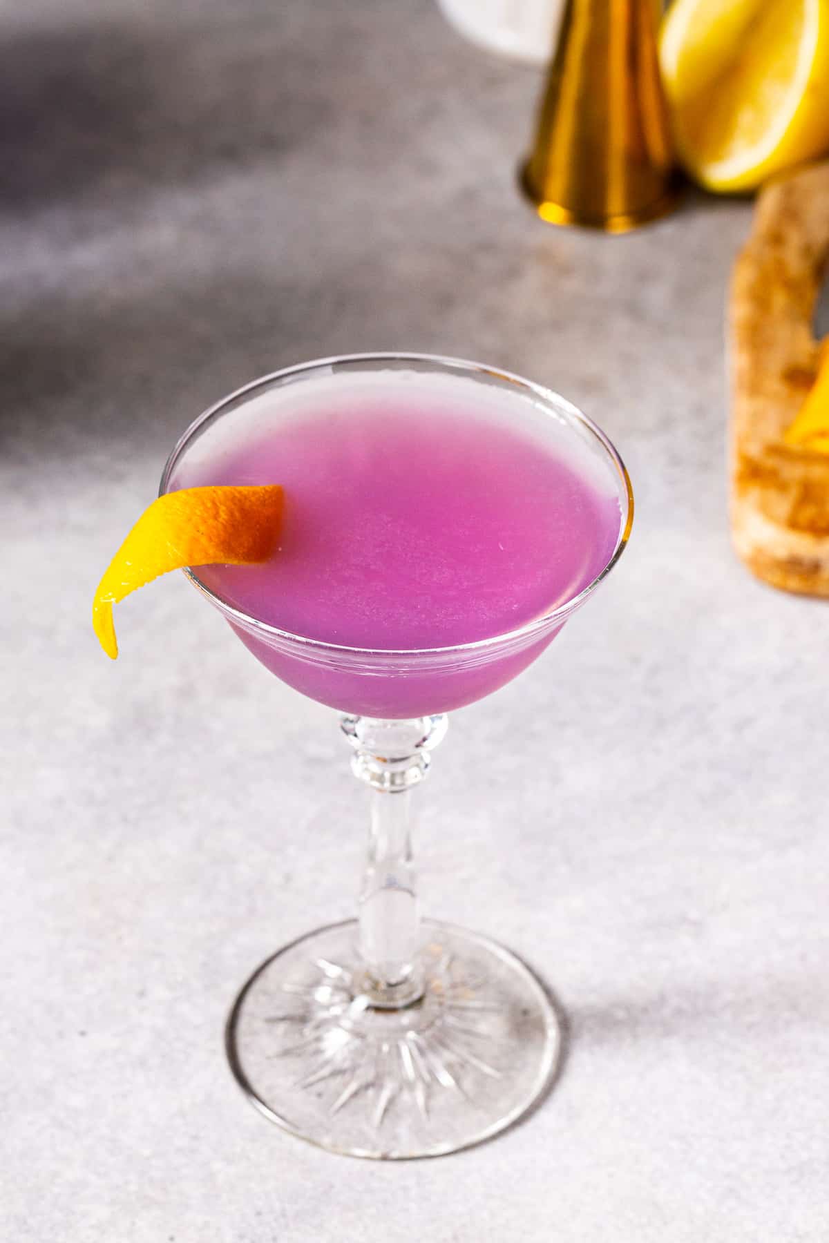 Overhead view or a purple Water lily cocktail in a coupe glass with an orange peel garnish.