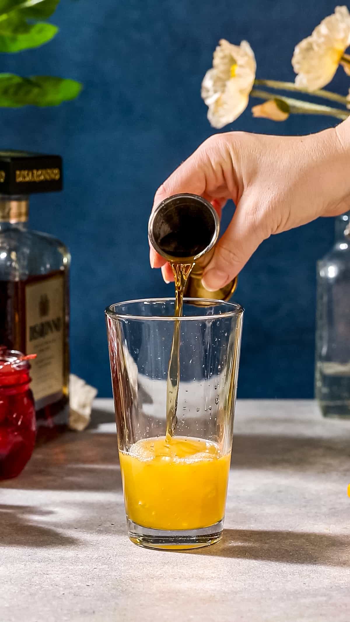 Pouring the amaretto into the cocktail shaker glass.