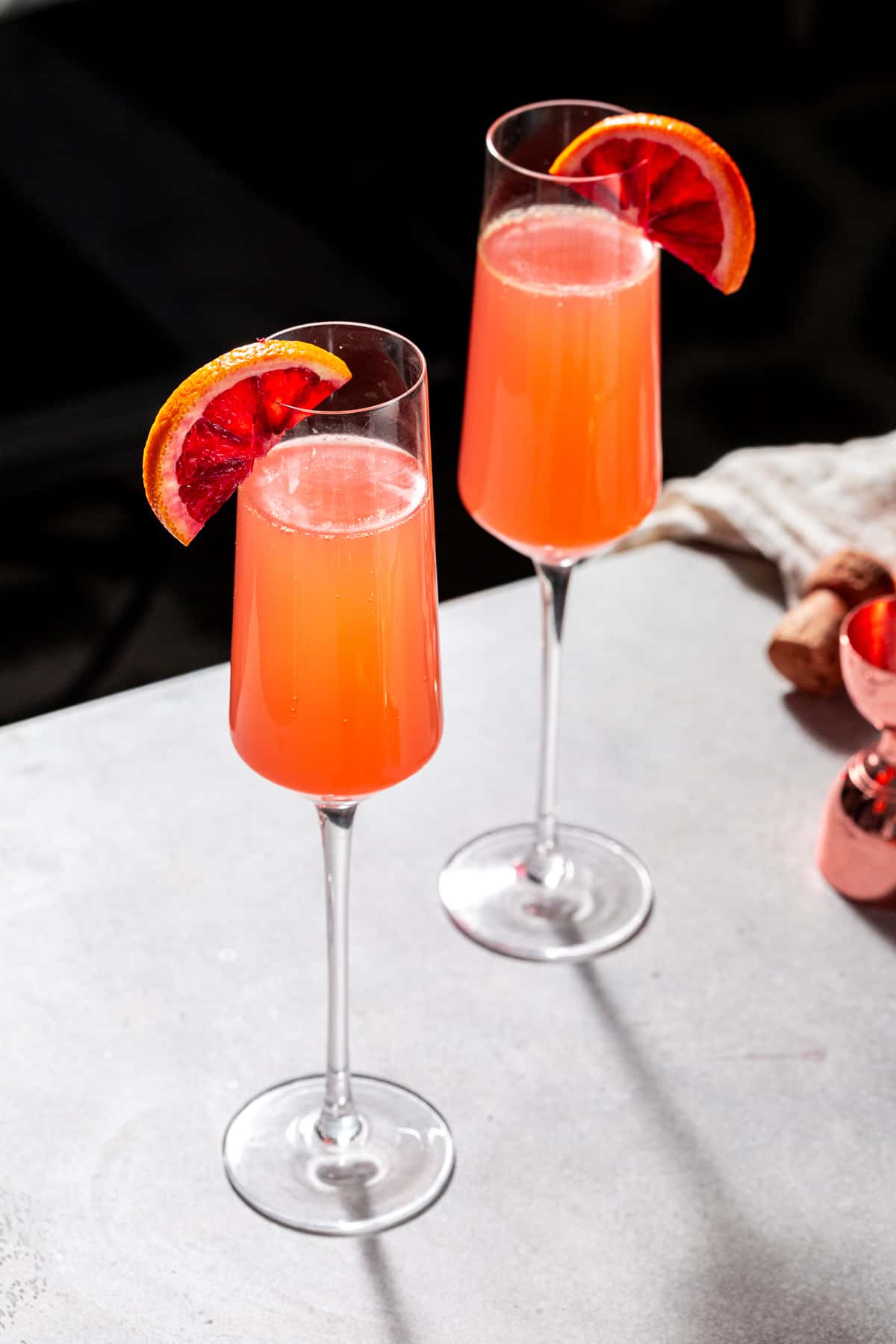 Overhead view of two blood orange mimosas on a countertop with light streaming in from behind.