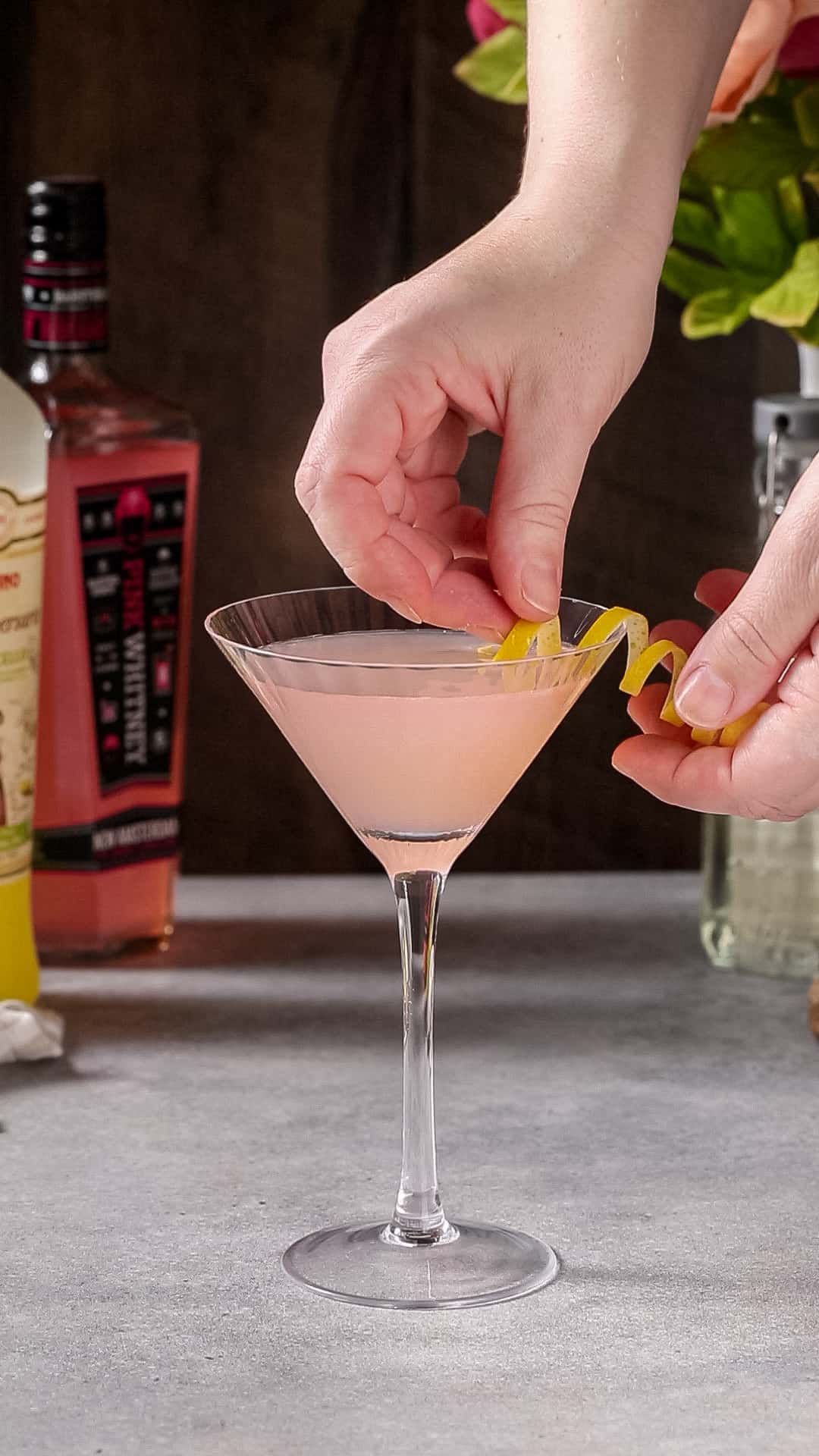 Garnishing a pink lemon drop martini with a lemon spiral.