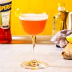 A prepared Aperol sour garnished with a lemon peel.