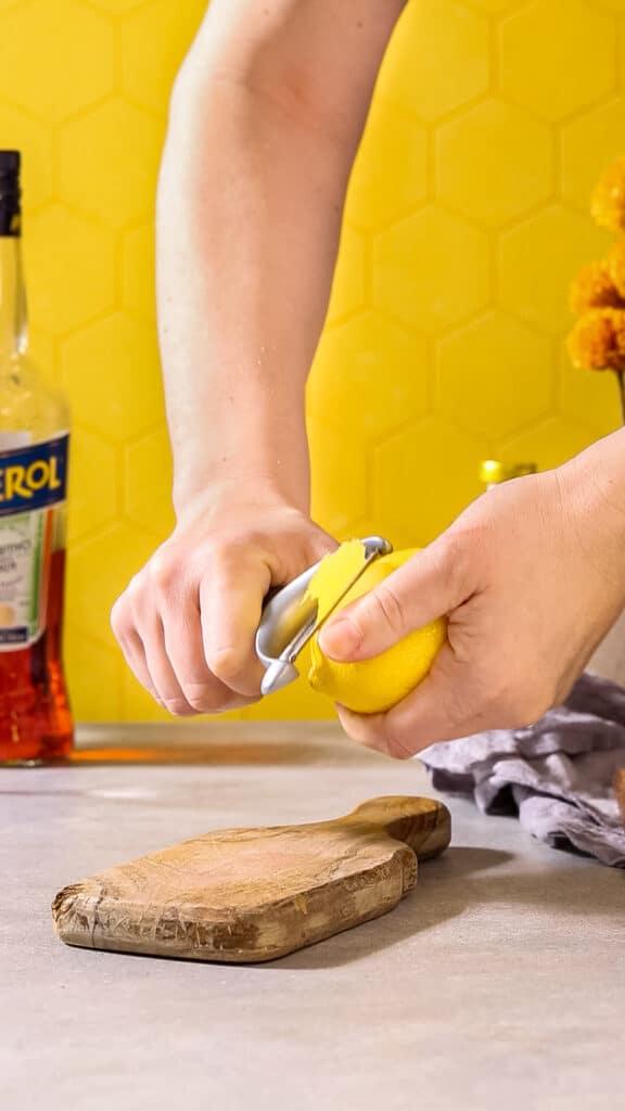 Using a vegetable peeler to peel a lemon.