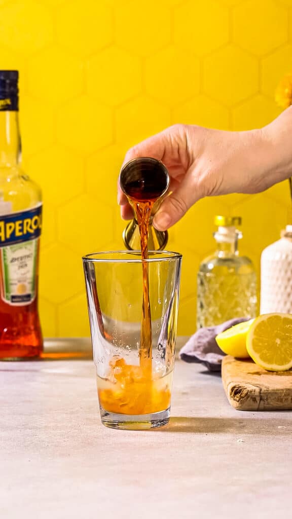 Adding Aperol to the cocktail glass.