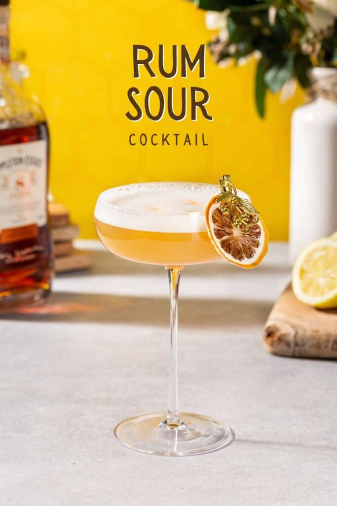 Side view of a Rum sour cocktail with a yellow background. Text at the top says "rum sour cocktail".
