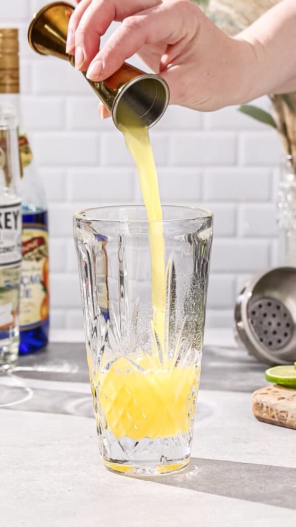 Hand adding pineapple juice to a cocktail shaker.