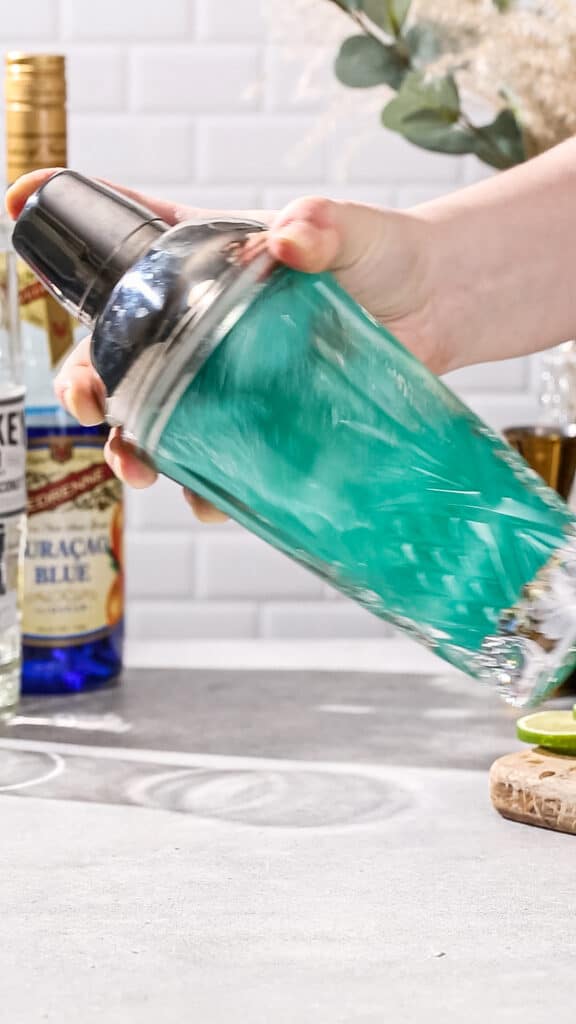 Hand shaking a cocktail shaker filled with blue liquid.