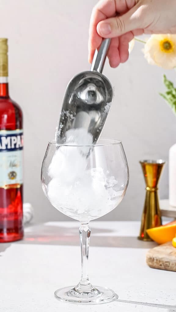 Hand using an ice scoop to add ice to a stemmed cocktail glass.