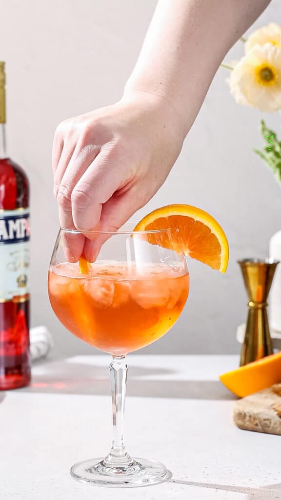 Hand adding a half orange slice to a cocktail glass.