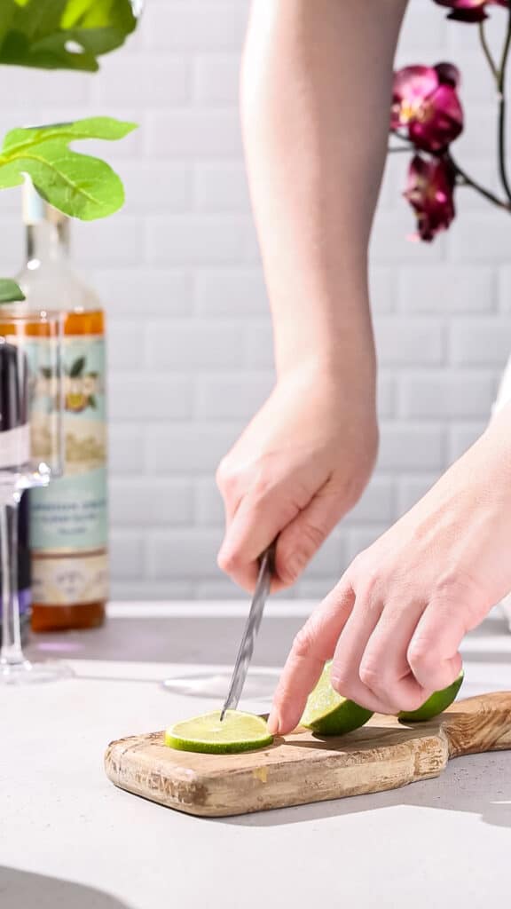 Hands using a knife to cut a slit in a slice of fresh lime.