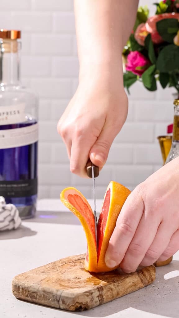 Hands using a knife to cut a slice of pink grapefruit.