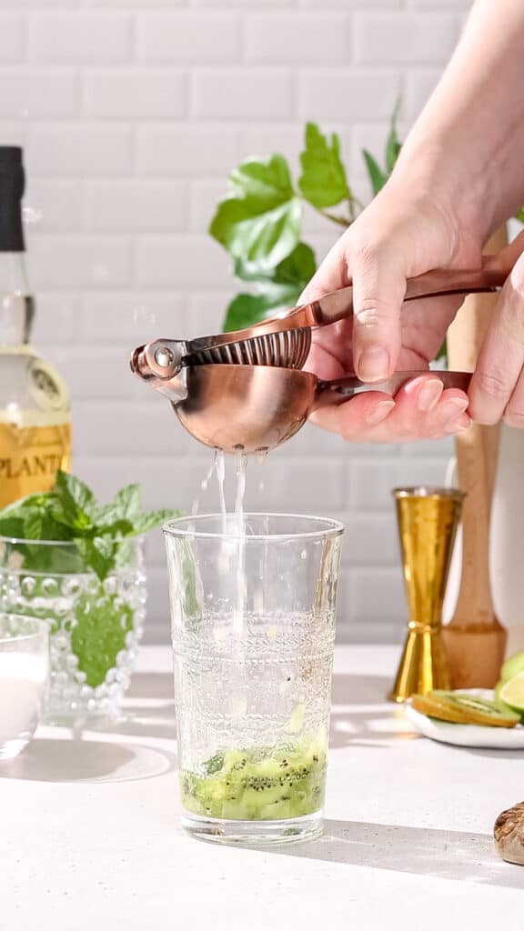 Hand using a copper colored citrus juicer to squeeze fresh lime juice into a cocktail glass.