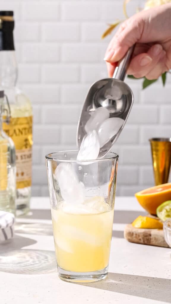 Hand using an ice scoop to fill a cocktail shaker with ice.