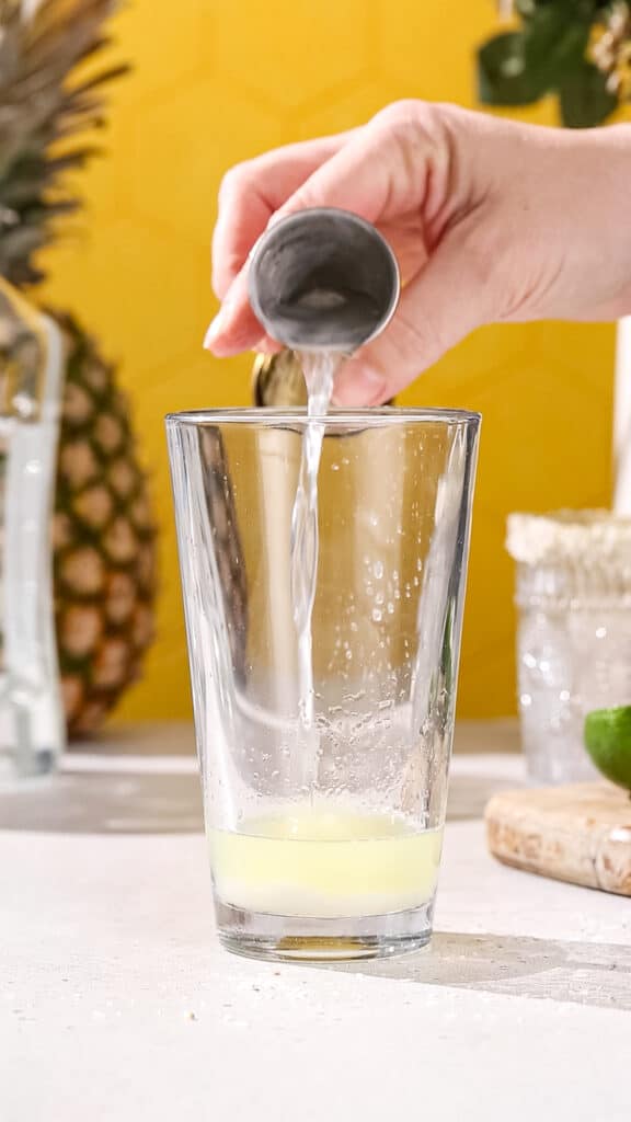 Hand pouring triple sec liqueur into a cocktail shaker.