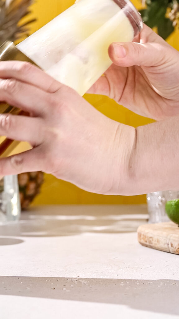 Close up of hands shaking up a cocktail using a cocktail shaker.