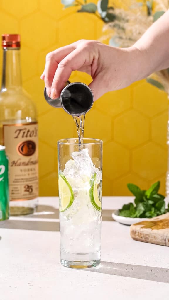 Hand using a jigger to pour vodka into a cocktail glass.