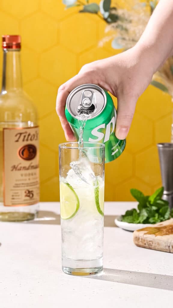 Hand pouring Sprite into a cocktail glass from a can.