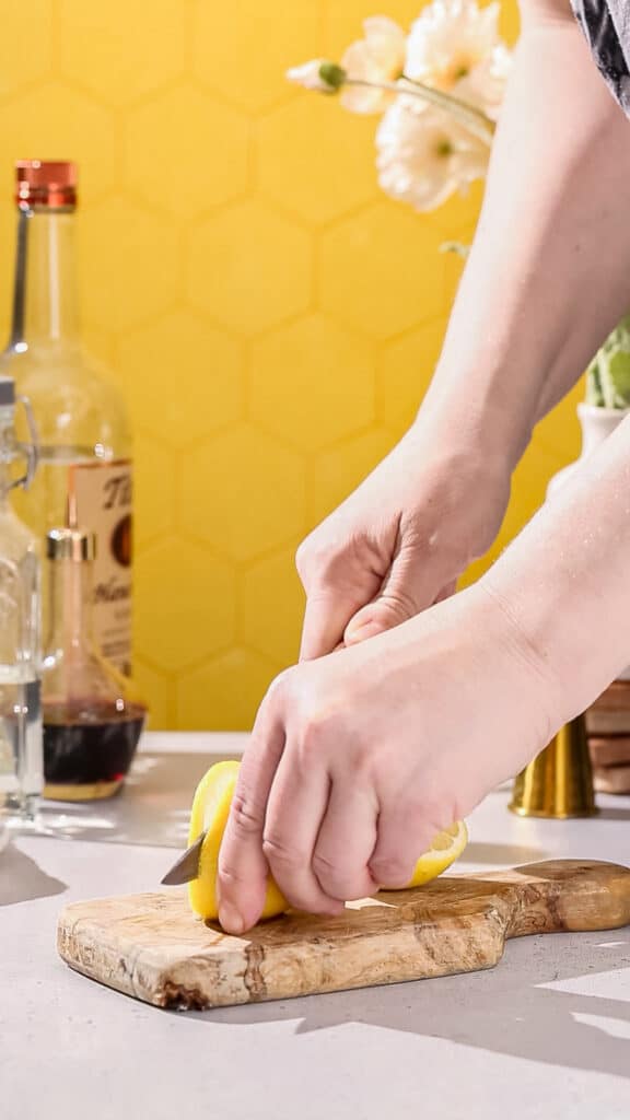Hands cutting a lemon slice to make a cocktail garnish.