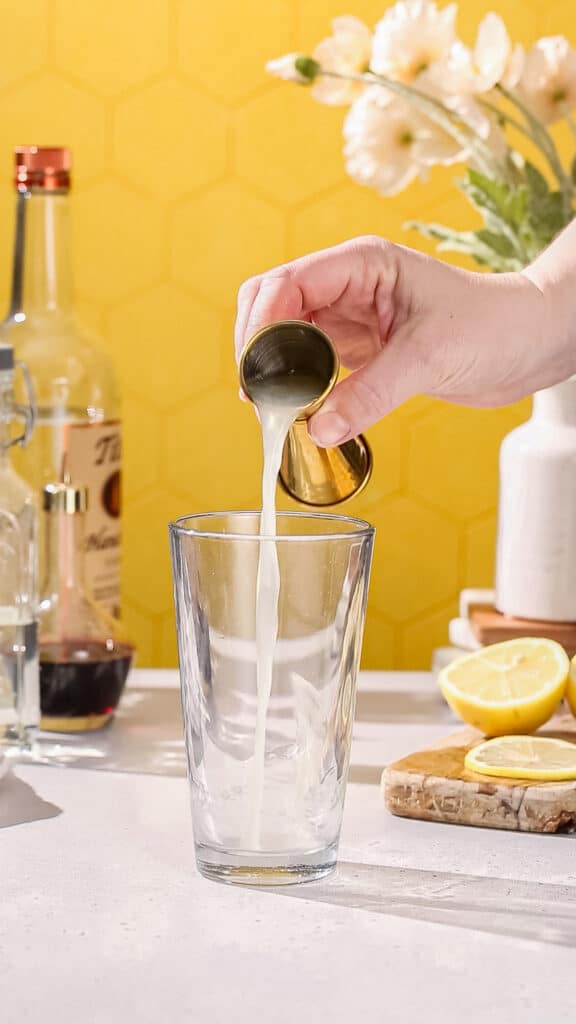Hand adding lemon juice to a cocktail shaker.