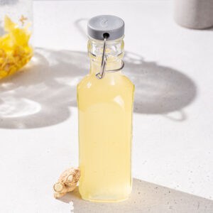 Slightly overhead view of ginger shrub in a bottle. A piece of ginger is next to it.